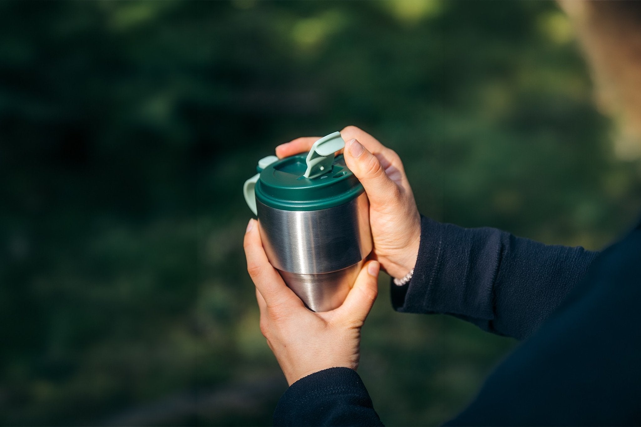 Thermobecher mit dunkelgrünem Snap-Deckel und geöffneter Klapplasche in der Hand